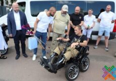 Group of men gathered around a man in a motorized wheelchair outdoors near a white van.