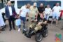 Group of men gathered around a man in a motorized wheelchair outdoors near a white van.