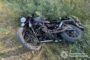 Black motorcycle lying on its side in tall grass, front wheel toward the camera; Ukrainian police watermark in the bottom right corner.