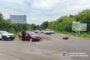 Police at a two-vehicle crash on a rural road: a red car with cones around it, a motorcycle on its side ahead, several bystanders and vehicles in the distance.