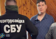 Back view of a man in a black jacket labeled 'контррозвідка СБУ' (SBU counterintelligence) standing in a wooden room with another man whose face is blurred.