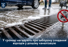 У центрі зливний решітчастий каналізаційний люк на вулиці; знак заборони скидати відходи до дощової каналізації; лого Хмельницької міської ради на панелі зверху