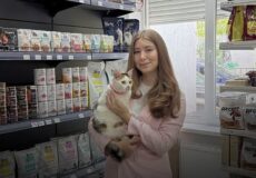 Woman holding a cat in a pet store, smiling, with product shelves behind and logos above, Ukrainian caption about an employment service project.
